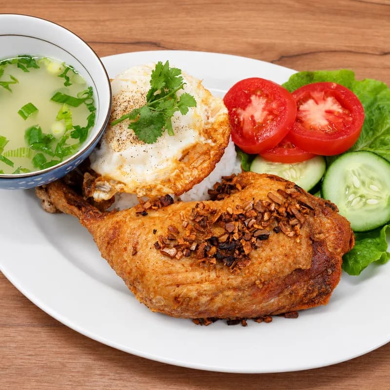 Grilled chicken leg over rice with a fried egg, tomato and cucumber