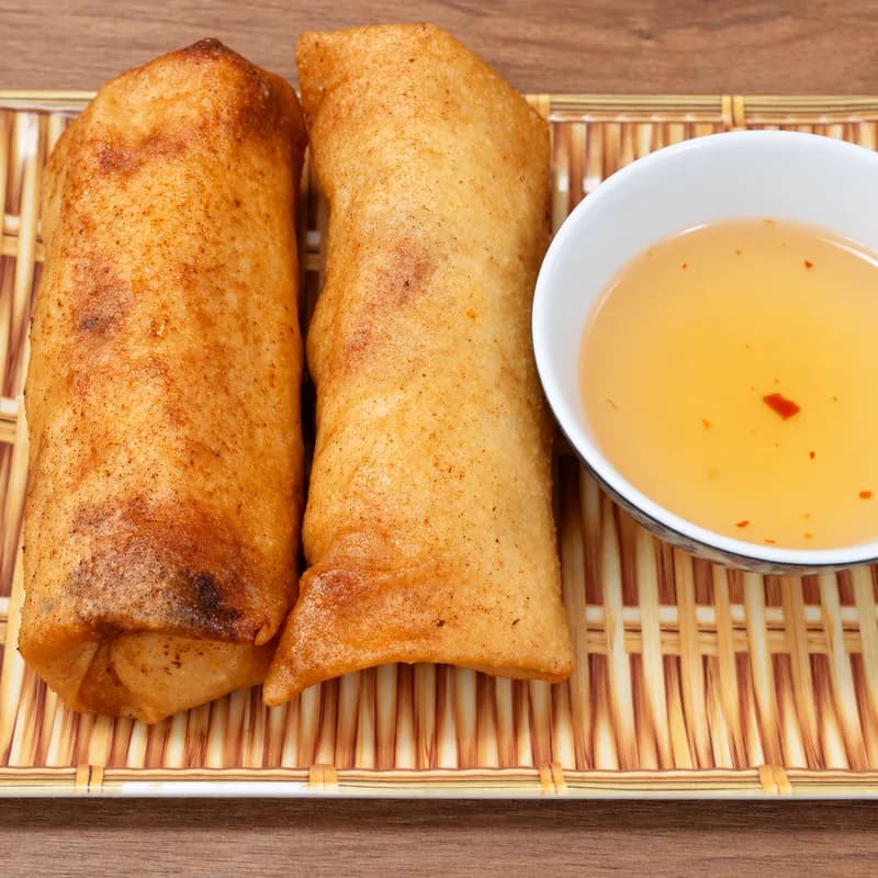 Two golden Vietnamese egg rolls on a bamboo tray with fish sauce